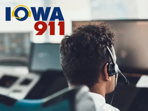 911 dispatcher looks at monitor, Iowa 911 logo.