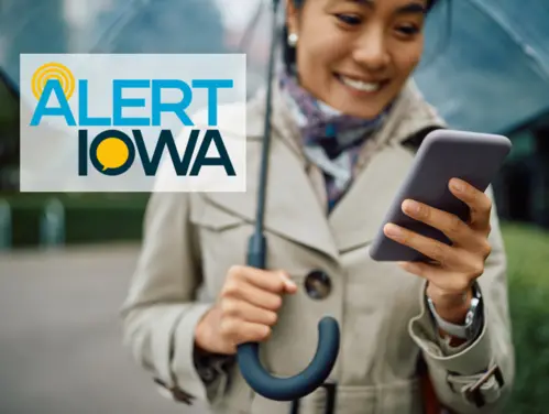 Woman walking with umbrella looks at phone, Alert Iowa logo.