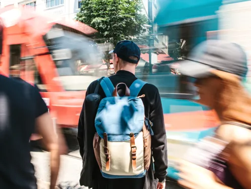 Blurry image of people on street and man with backpack crossing traffic.