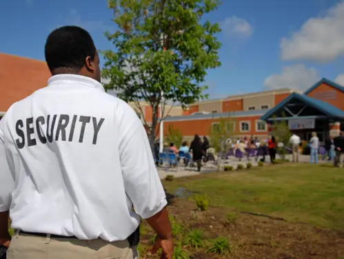 Male Security Officer looks on at kids and teachers walking into school.
