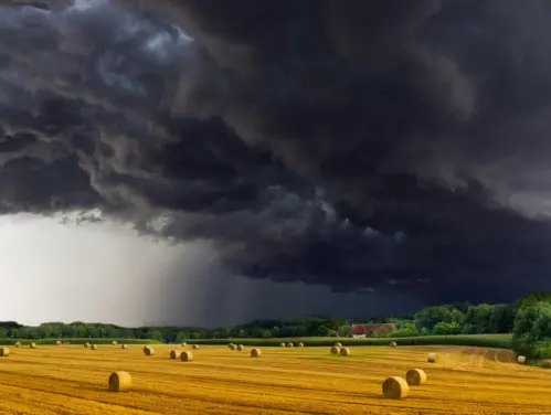 Dark storm clouds form over field with hay bails. 