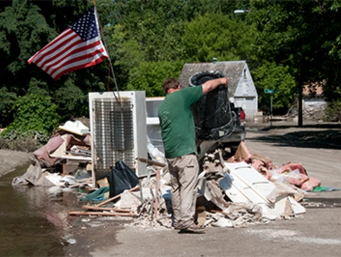 Man hauls out flooded house items to the street to be disposed.