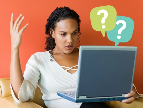 Woman looking confused at laptop with question marks.