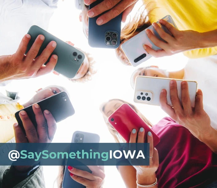 People on cell phones using social media in a circle. Text: @SaySomething Iowa.