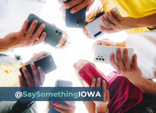 People on cell phones using social media in a circle. Text: @SaySomething Iowa.