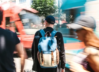 Blurry image of people on street and man with backpack crossing traffic.