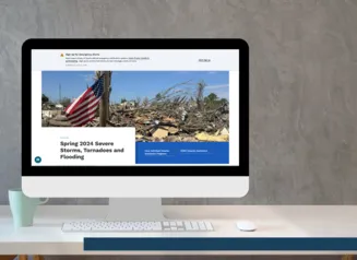 A white desk is shown with a desktop computer open to the Disaster Recovery Website set against a grey background. 