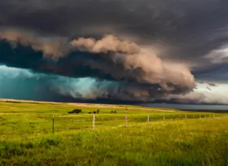 Dark clouds from approaching thunderstorm hang over rural field.
