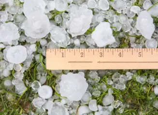 Pieces of hail spread out on ground with ruler measuring 1-2 inches on some hail.