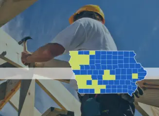 Man uses hammer on house roof. Text: State Disaster Housing Programs. Iowa county map with highlighted counties: Adair, Adams, Buena Vista, Cedar, Cherokee, Clarke, Clay, Emmet, Harrison, Jasper, Lyon, Mills, Montgomery, O’Brien, Plymouth, Polk, Pottawattamie, Ringgold, Shelby, Sioux, Story, Union and Woodbury.