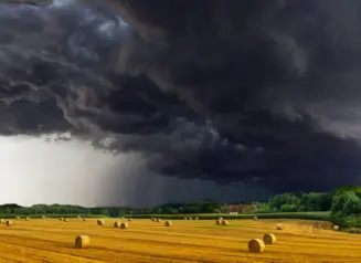 Dark storm clouds form over field with hay bails. 