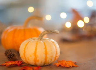 Pumpkins and fall leaves on table with holiday lighting.