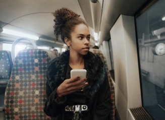Woman looks out train window with phone in hand.
