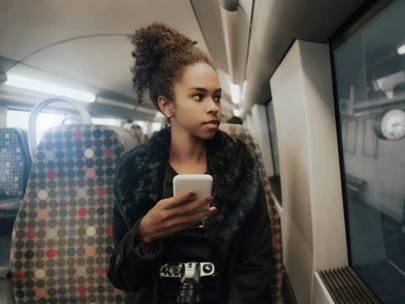 Woman looks out train window with phone in hand.